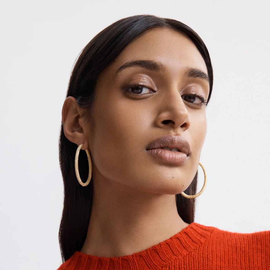 Model wearing large oval hoop gold earrings