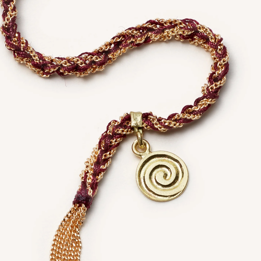 Closeup of burgundy silk and gold rope bracelet with gold circle swirl charm