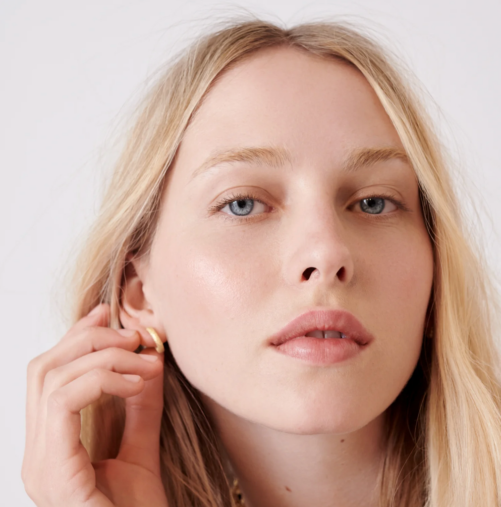 Model wearing oval gold florentine finish huggy earrings