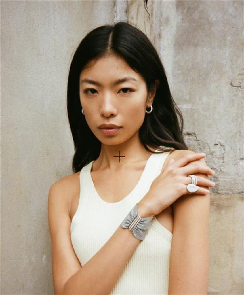 model wearing round gold huggy earrings and white gold woven bracelet