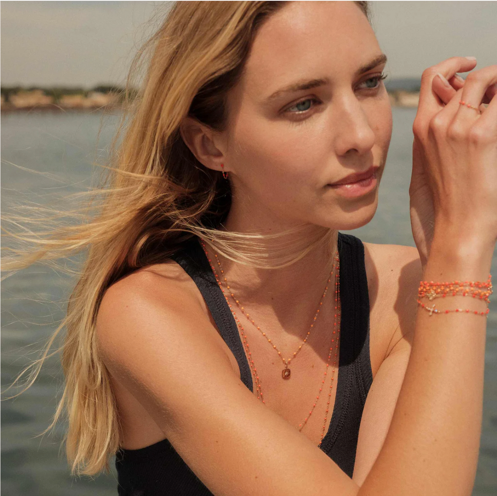 model wearing dainty coral beaded bracelets and necklaces with varying gold charms