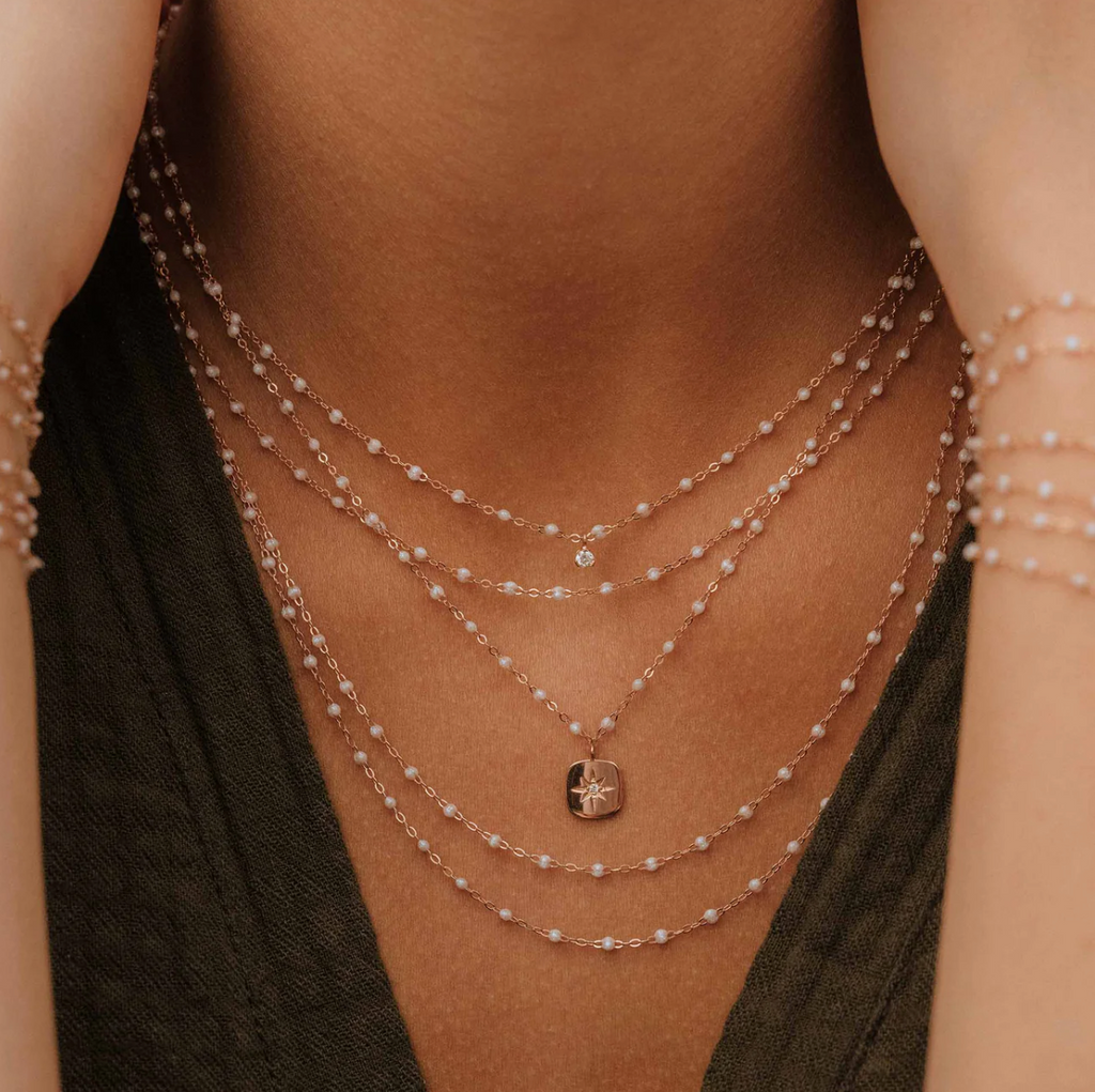 model wearing multiple dainty white beaded and gold necklaces with one diamond charm and one gold with star and diamond center charm