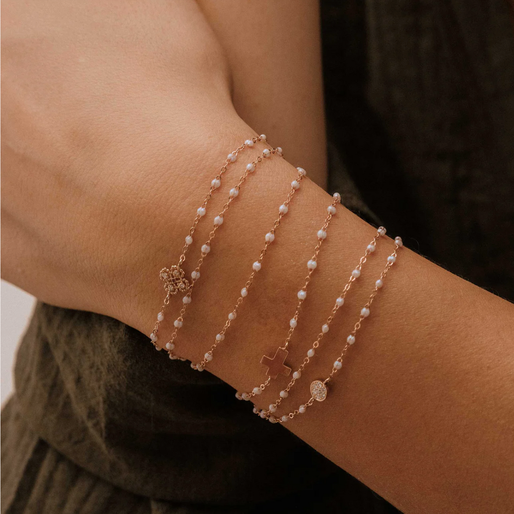 model wearing 6 dainty gold and white beaded bracelets with cross, diamond, and clover centers
