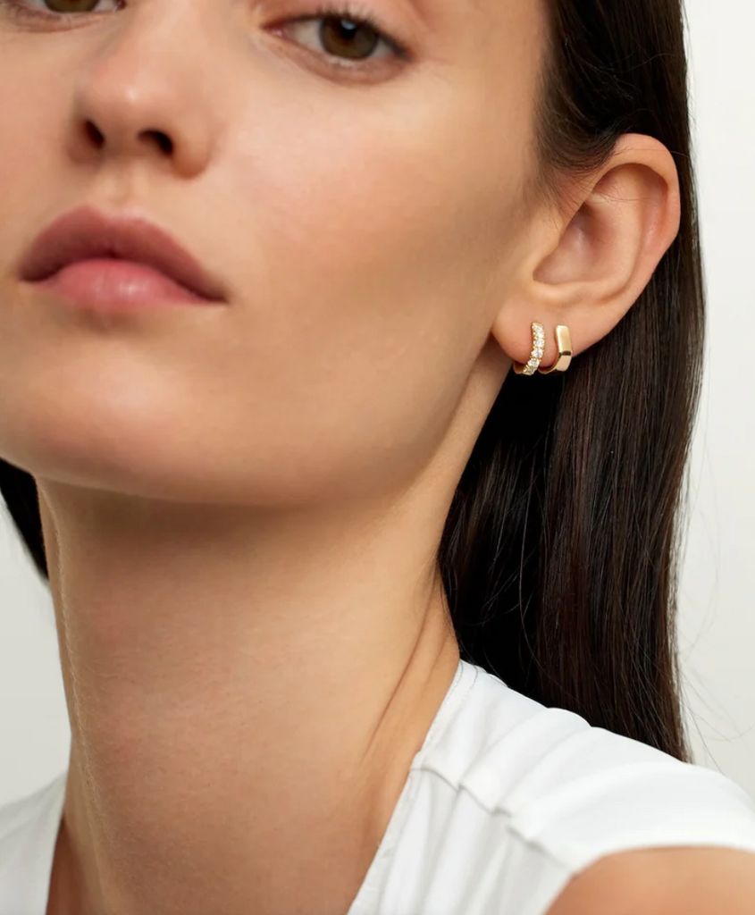 Close-up of a woman wearing gold hoop earrings with a neutral background