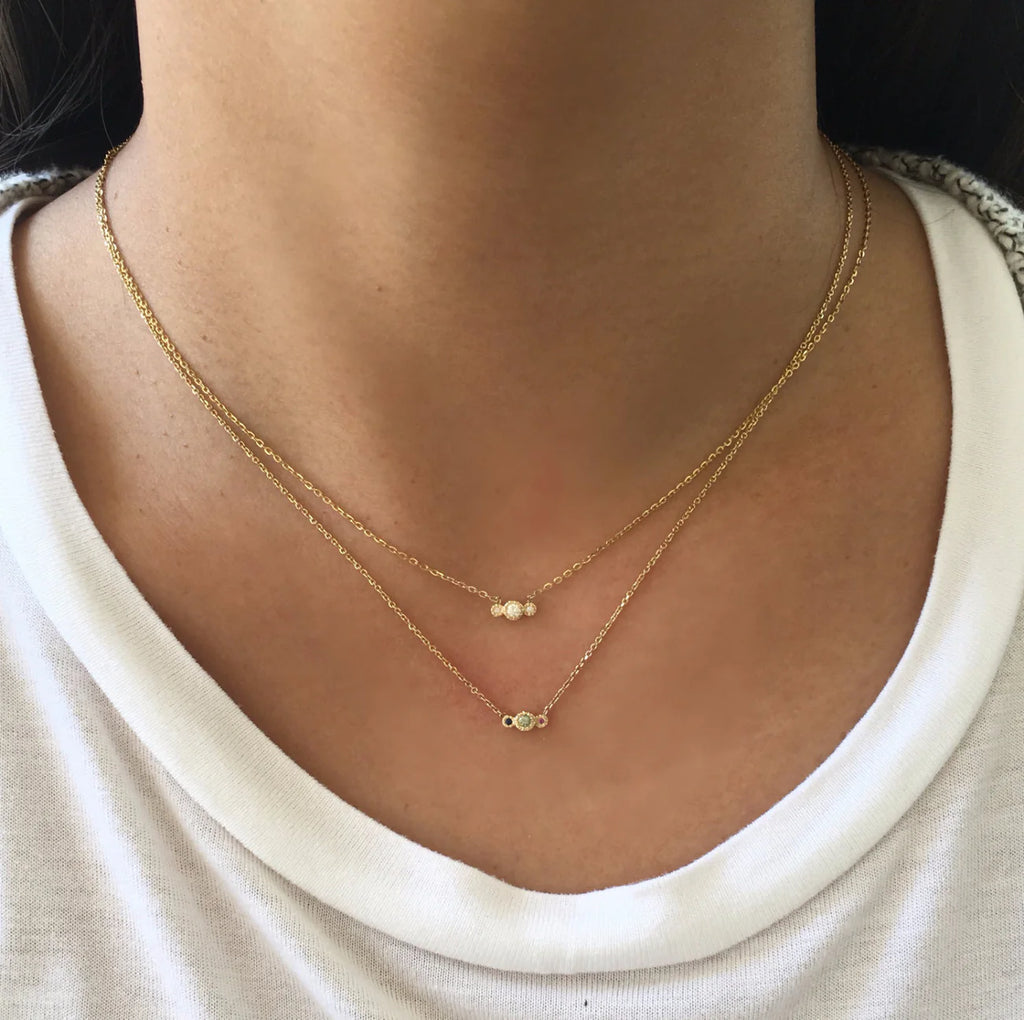 model wearing 2 necklaces one with 3 diamonds and one with 3 gemstones