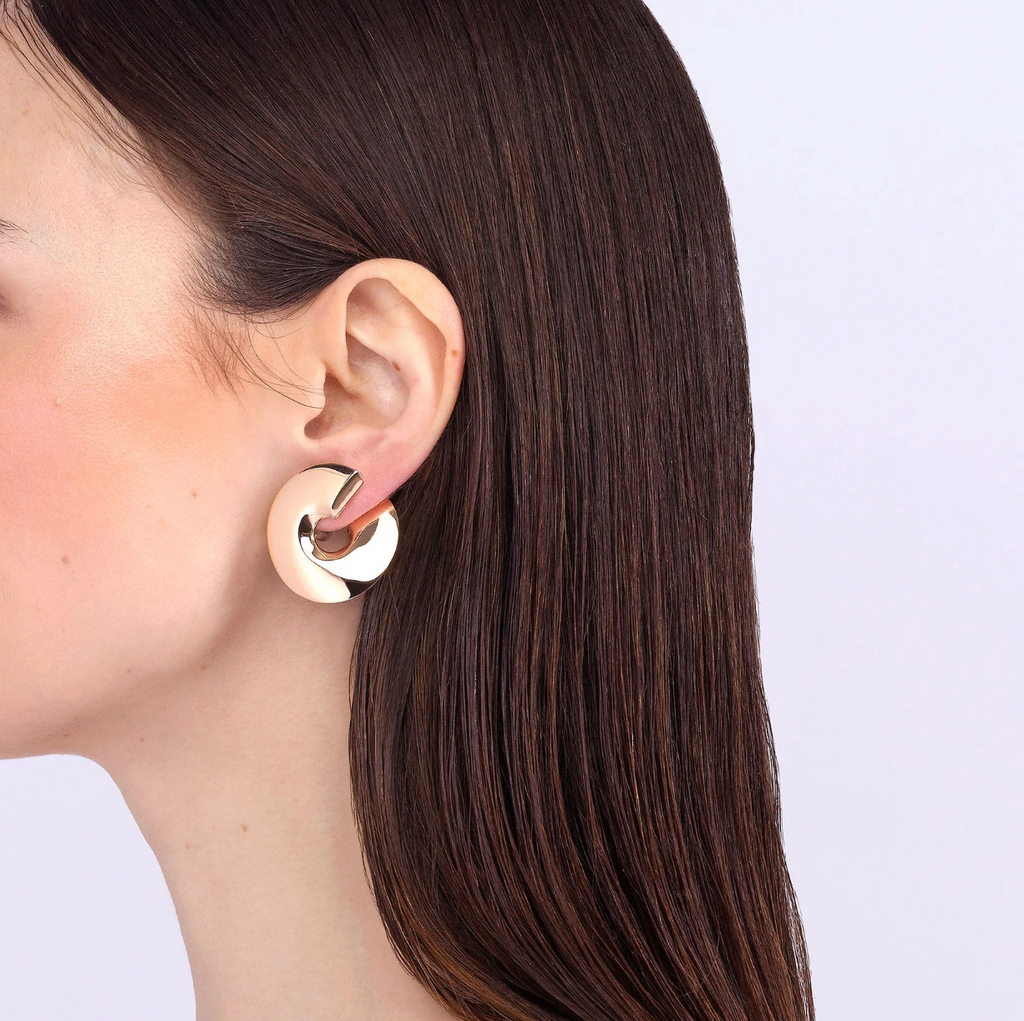 Close-up of a person wearing a gold hoop earring on a plain background